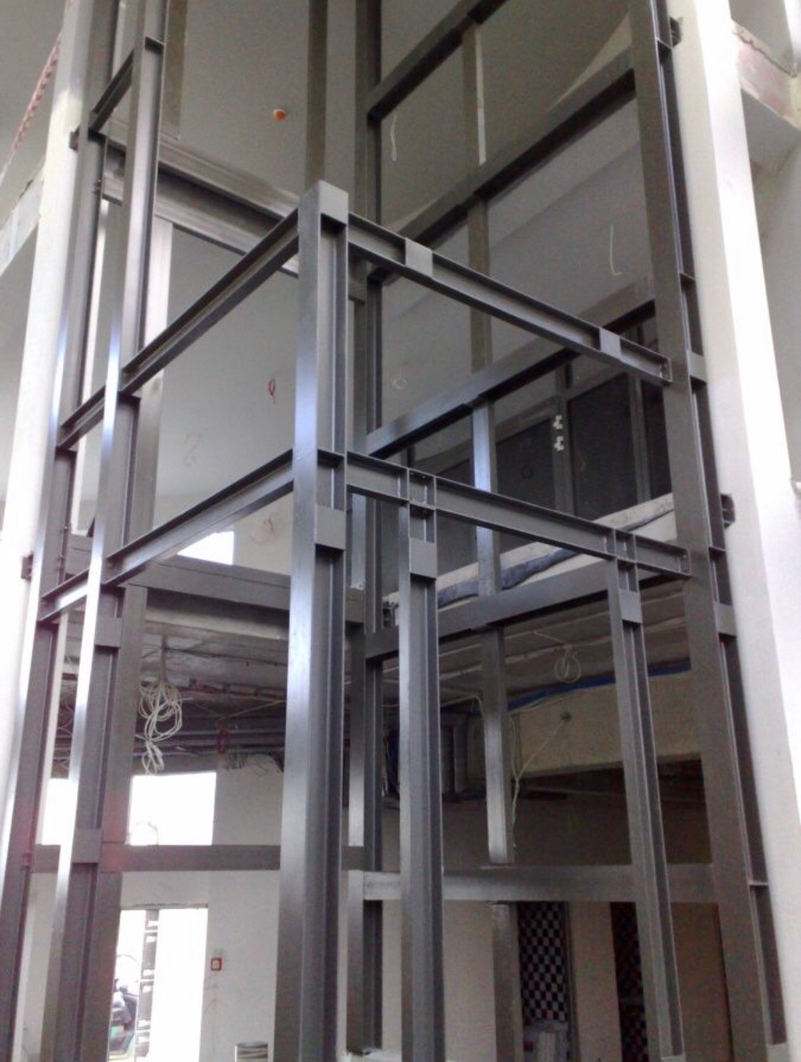 Surowa, stalowa konstrukcja nośna wewnątrz budynku w trakcie budowy, widoczne kable i instalacje na suficie, pionowy kadr.