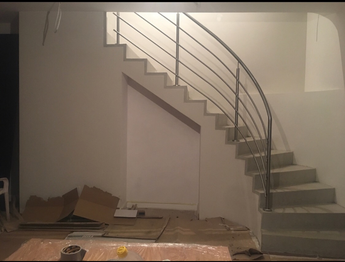 Montaż poręczy ze stali nierdzewnej przy schodach w trakcie remontu, widoczne kartony i folia ochronna na podłodze.