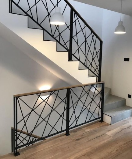 Schody wewnętrzne z nowoczesną balustradą z czarnych prętów tworzących geometryczny wzór, drewniany pochwyt, oświetlenie punktowe