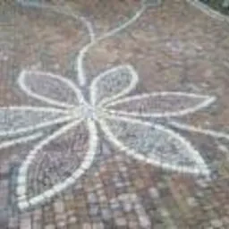 Wzór kwiatowy ułożony z jasnoszarej kostki na brązowo-beżowej nawierzchni z kostki, widok z góry.