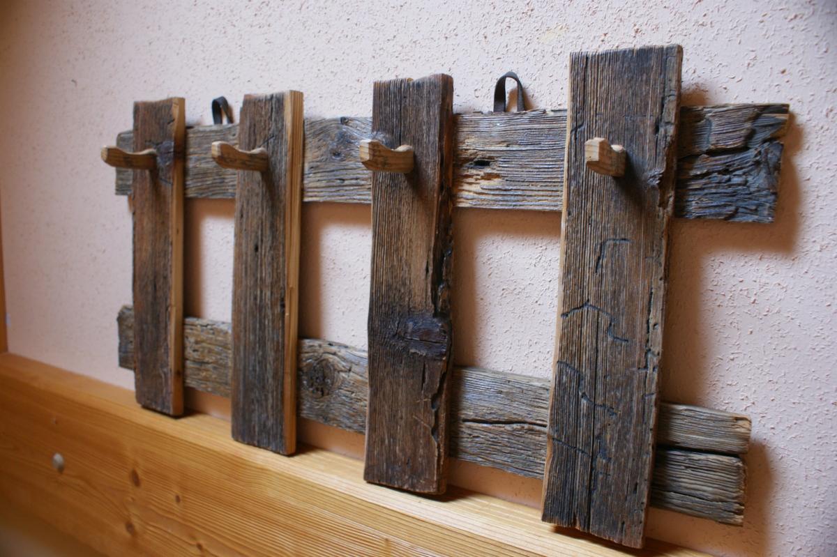 Ręcznie robiony wieszak z surowego, postarzanego drewna z czterema haczykami, montowany na ścianie nad drewnianą półką. Widoczne sęki i naturalne pęknięcia drewna.