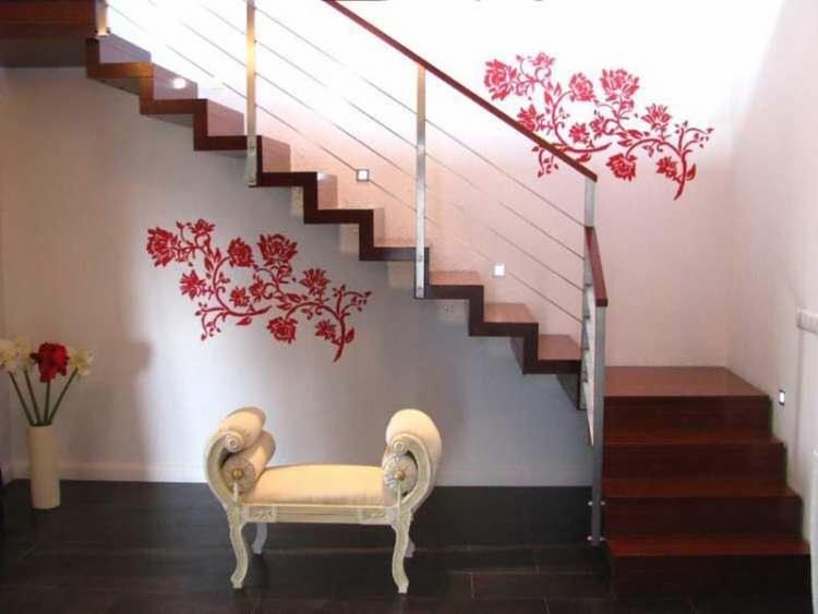 Nowoczesne schody drewniane z metalową balustradą, ozdobione kwiatowymi naklejkami ściennymi. U dołu kremowa ławeczka z dekoracyjnymi podłokietnikami.