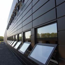 BOB ROLLO Sp. z o.o. - Czarne okna PCV uchylne w nowoczesnym budynku biurowym z elewacją z paneli. Widok z dołu, okna częściowo otwarte, odbijają światło.