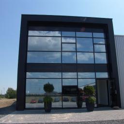 BOB ROLLO Sp. z o.o. - Nowoczesna fasada budynku z dużymi, aluminiowymi oknami, w których odbija się błękitne niebo. Przed wejściem ustawione dekoracyjne rośliny w donicach.