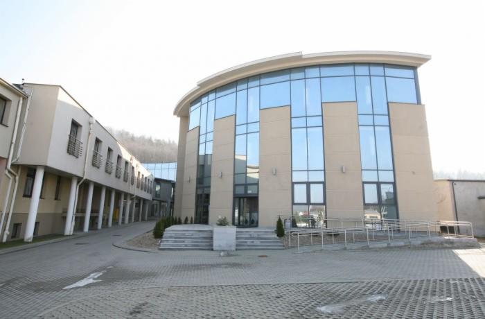 Nowoczesny budynek z fasadą ze szkła i beżu, z rampą dla niepełnosprawnych i chodnikiem z kostki brukowej. Widok z zewnątrz, jasne oświetlenie.