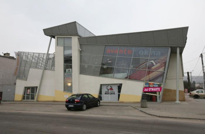 Salon sprzedaży okien i drzwi o nowoczesnej architekturze, z dużymi przeszkleniami i napisem 'avante okna'. Na parkingu stoi ciemny samochód.