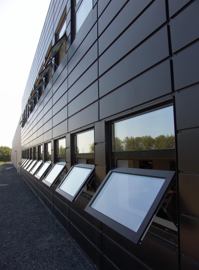 Czarne okna PCV uchylne w nowoczesnym budynku biurowym z elewacją z paneli. Widok z dołu, okna częściowo otwarte, odbijają światło.