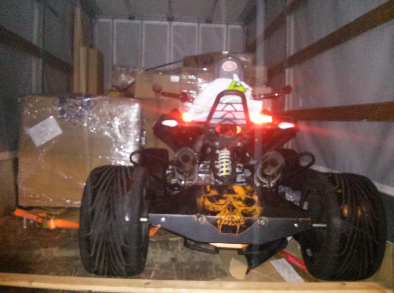 ATV z motywem czaszki, zabezpieczone pasami wewnątrz przestrzeni ładunkowej busa, gotowe do transportu. Widoczne kartony i elementy mocujące.