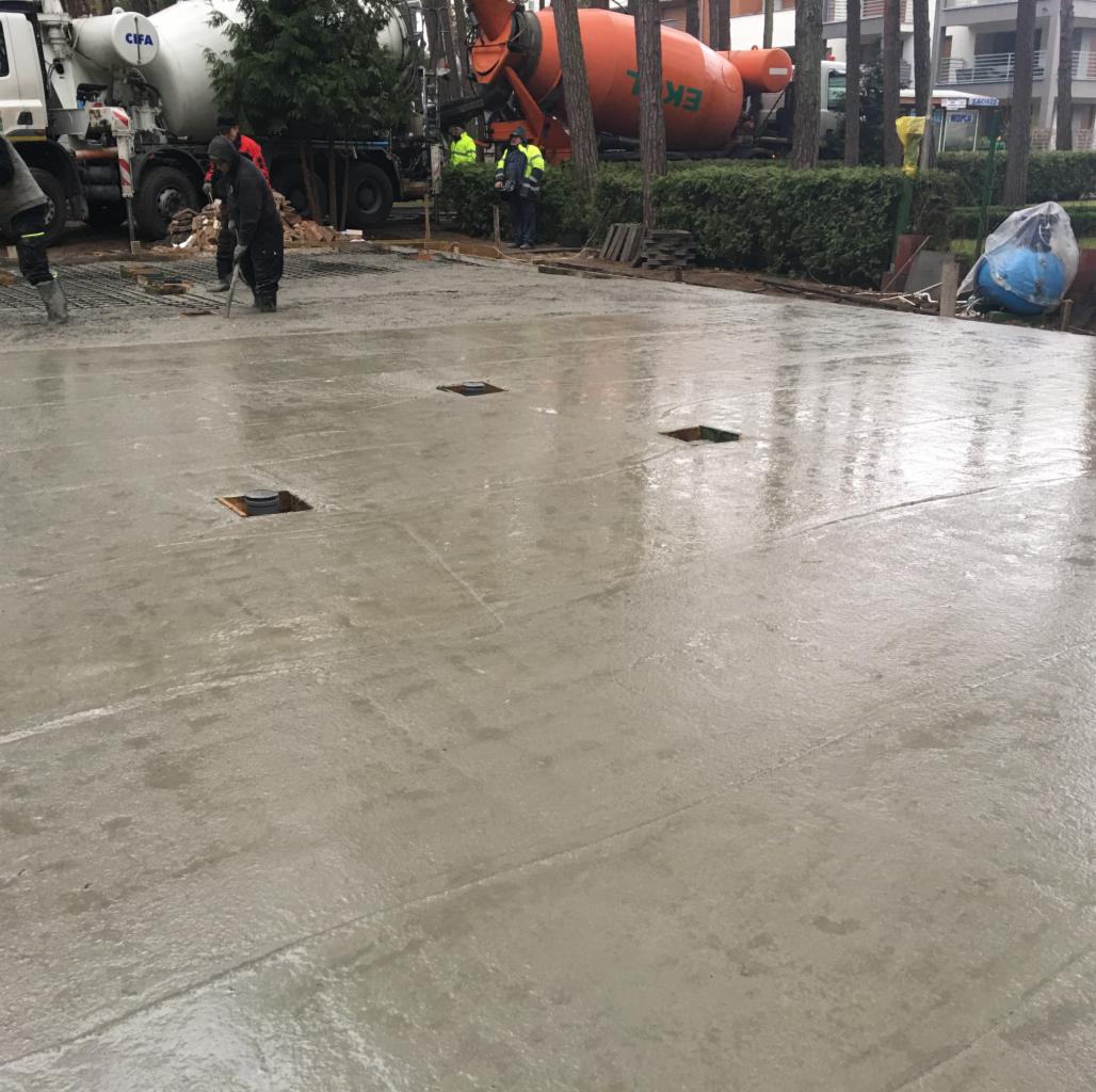 Wylewka betonowa w trakcie realizacji, widoczne zbrojenia, pracownicy w odblaskowych kamizelkach i betoniarki w tle.