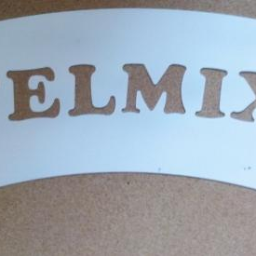 PPHU Felmix - Wycięty laserowo, zakrzywiony element z nazwą firmy 'FELMIX', wykonany z jasnego metalu na brązowym tle. Precyzyjna obróbka CNC.