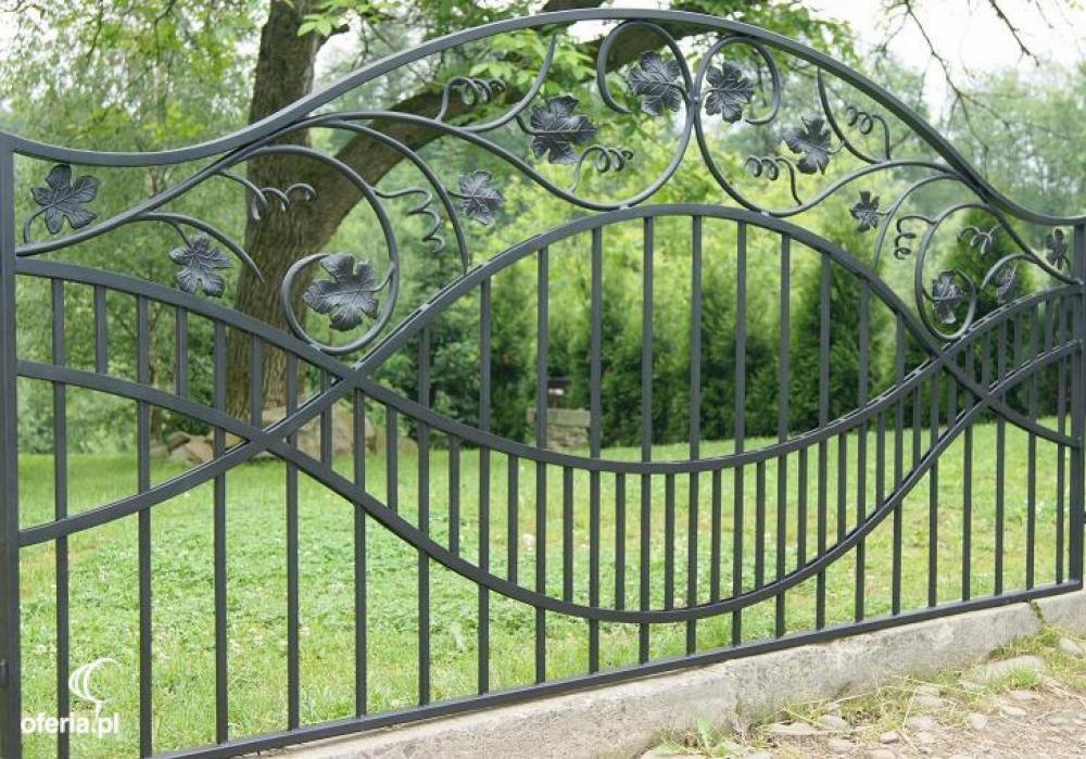 Kute, czarne ogrodzenie z motywem liści winogron na tle zielonego trawnika i drzew. Dekoracyjny, metalowy płot w stylu rustykalnym.