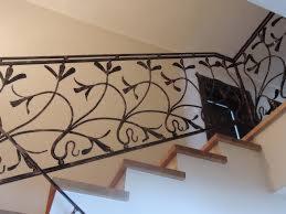 Kute, ciemne balustrady schodowe z motywem roślinnym, widoczne z dołu, w jasnym wnętrzu. Dekoracyjny detal architektoniczny.