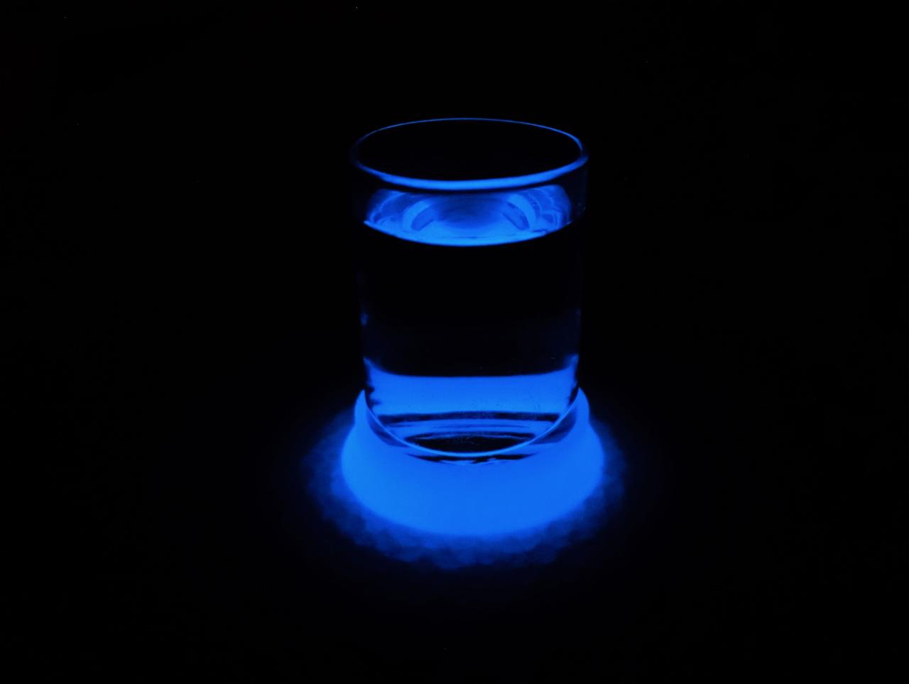 Szklanka wody podświetlona intensywnym niebieskim światłem na czarnym tle.