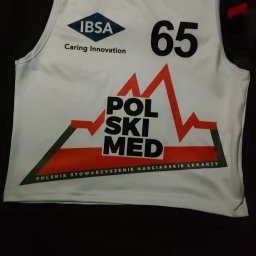 MASTERSON REKLAMA Fabryka.Form - Biała koszulka sportowa z logo IBSA, numerem 65 i napisem POLSKI MED, leżąca na czarnym tle. Koszulka Polskiego Stowarzyszenia Narciarskiego Lekarzy.