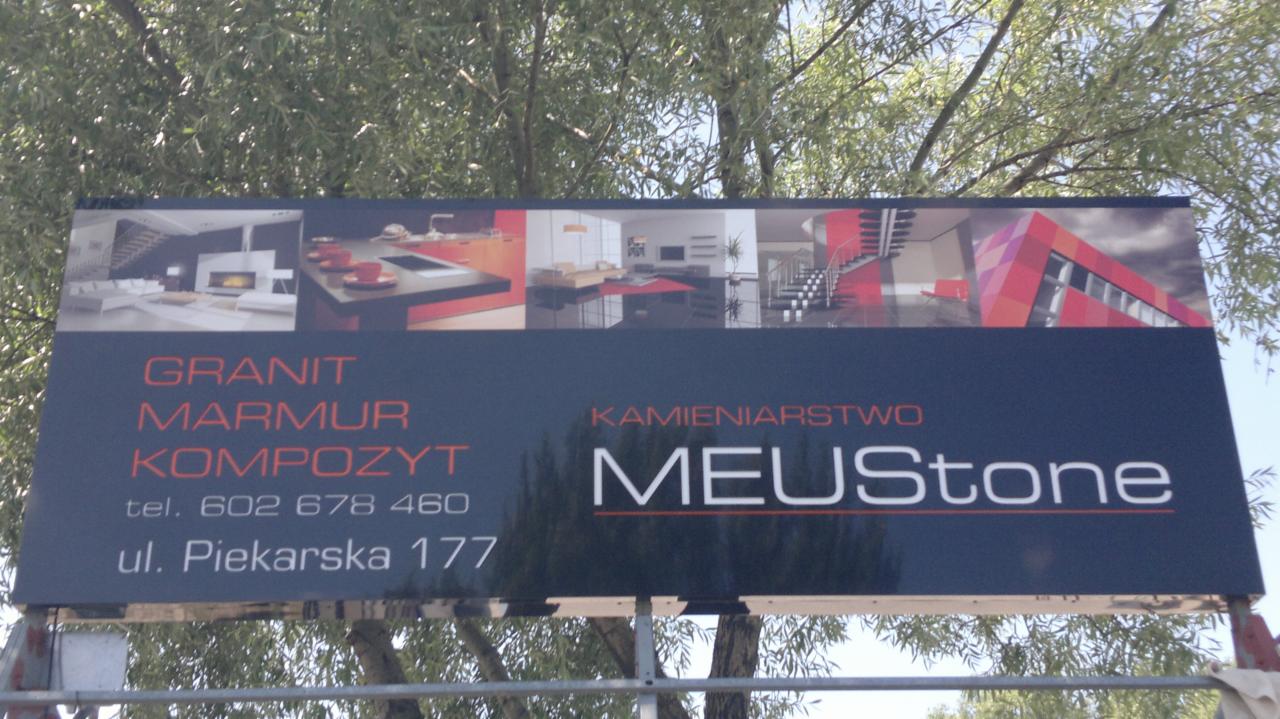 Billboard kamieniarski MEUStone z wizualizacjami wnętrz i elewacji z granitu, marmuru i kompozytu, numer telefonu i adres na tle drzew.