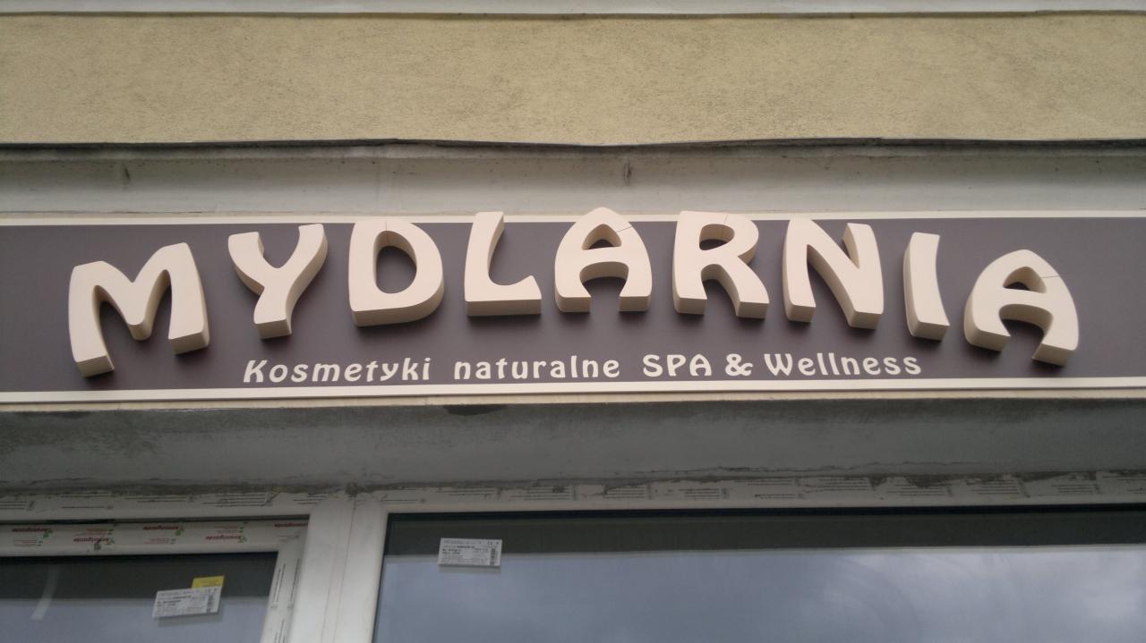 Elewacyjna tablica z napisem 'Mydlarnia' i dopiskiem 'Kosmetyki naturalne SPA & Wellness' nad witryną sklepu, wykonana z trójwymiarowych liter.