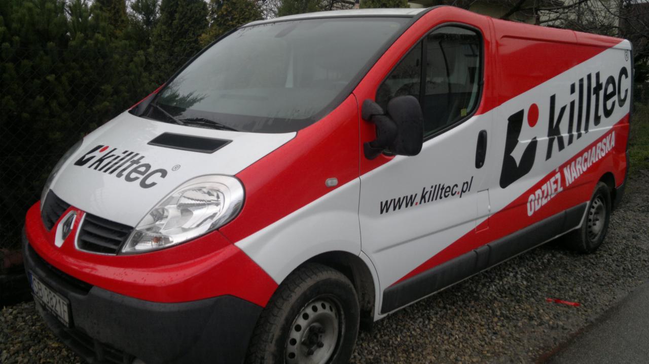 Biały van Renault Trafic z czerwonymi akcentami i brandingiem Killtec, zaparkowany na żwirowym podłożu. Widoczny adres strony internetowej firmy.