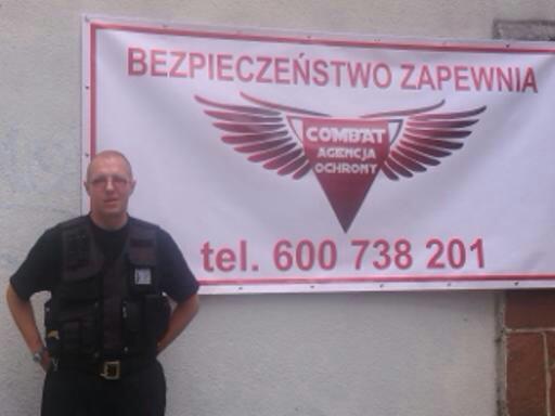 Pracownik agencji ochrony Combat w kamizelce taktycznej, pozujący na tle baneru reklamowego z numerem telefonu.