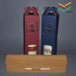 Dwa kartonowe opakowania na wino, jedno bordowe, drugie granatowe, z wyciętym motywem choinki i widoczną etykietą butelki wina, oraz drewniane pudełko z listewek na butelkę wina na pierwszym planie.