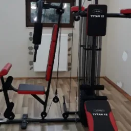 Wielofunkcyjna maszyna do ćwiczeń HMS Tytan 12 w domowym otoczeniu, z widocznym oknem w tle.