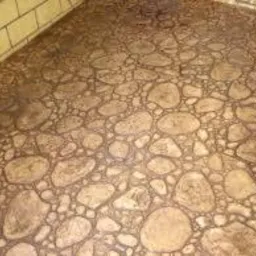 Wykończona posadzka imitująca kamienny bruk na tarasie z ceglaną ścianą. Realizacja z bliska, ukazująca detale wzoru i fakturę powierzchni.