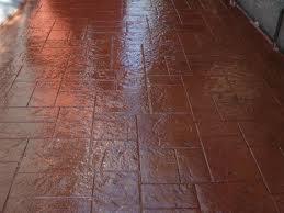 Ciemnobrązowa, błyszcząca posadzka imitująca kamień, ułożona we wzór prostokątów. Widoczne odbicie światła na powierzchni.