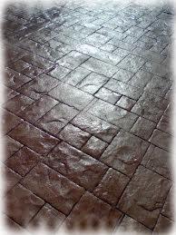 Szara, błyszcząca posadzka imitująca kamienną kostkę brukową, ułożona w geometryczny wzór. Powierzchnia lekko odbija światło, podkreślając fakturę.