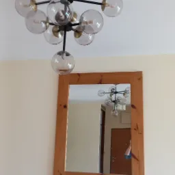 Nowoczesna lampa sufitowa z kulistymi kloszami, odbijająca się w lustrze z drewnianą ramą na kremowej ścianie. Widok z dołu, oświetlenie wnętrza.