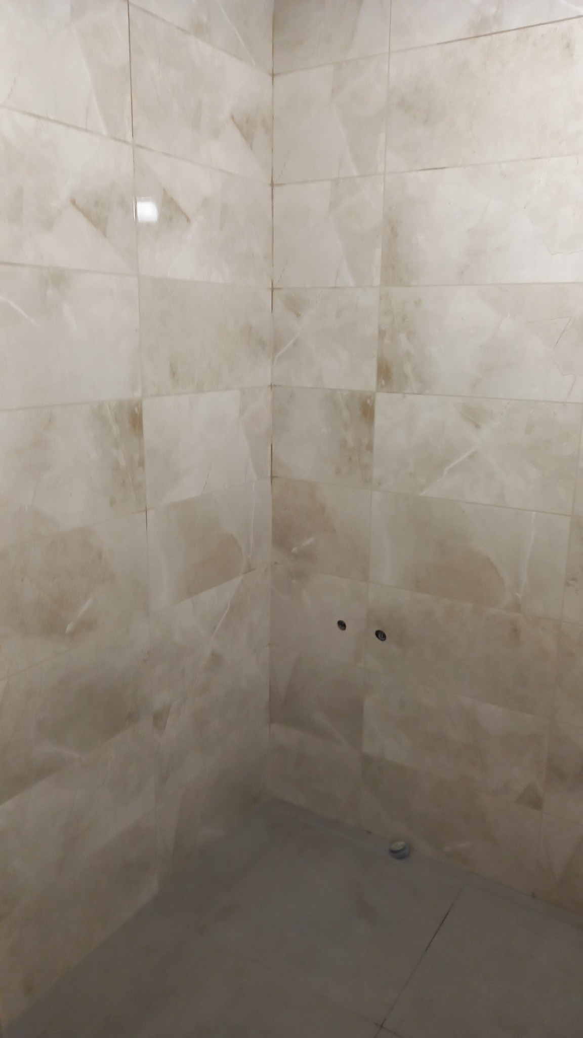 Wykończona łazienka z beżowymi, marmurkowymi płytkami na ścianach i podłodze. Widoczne otwory na baterię. Ukończony remont w neutralnej kolorystyce.