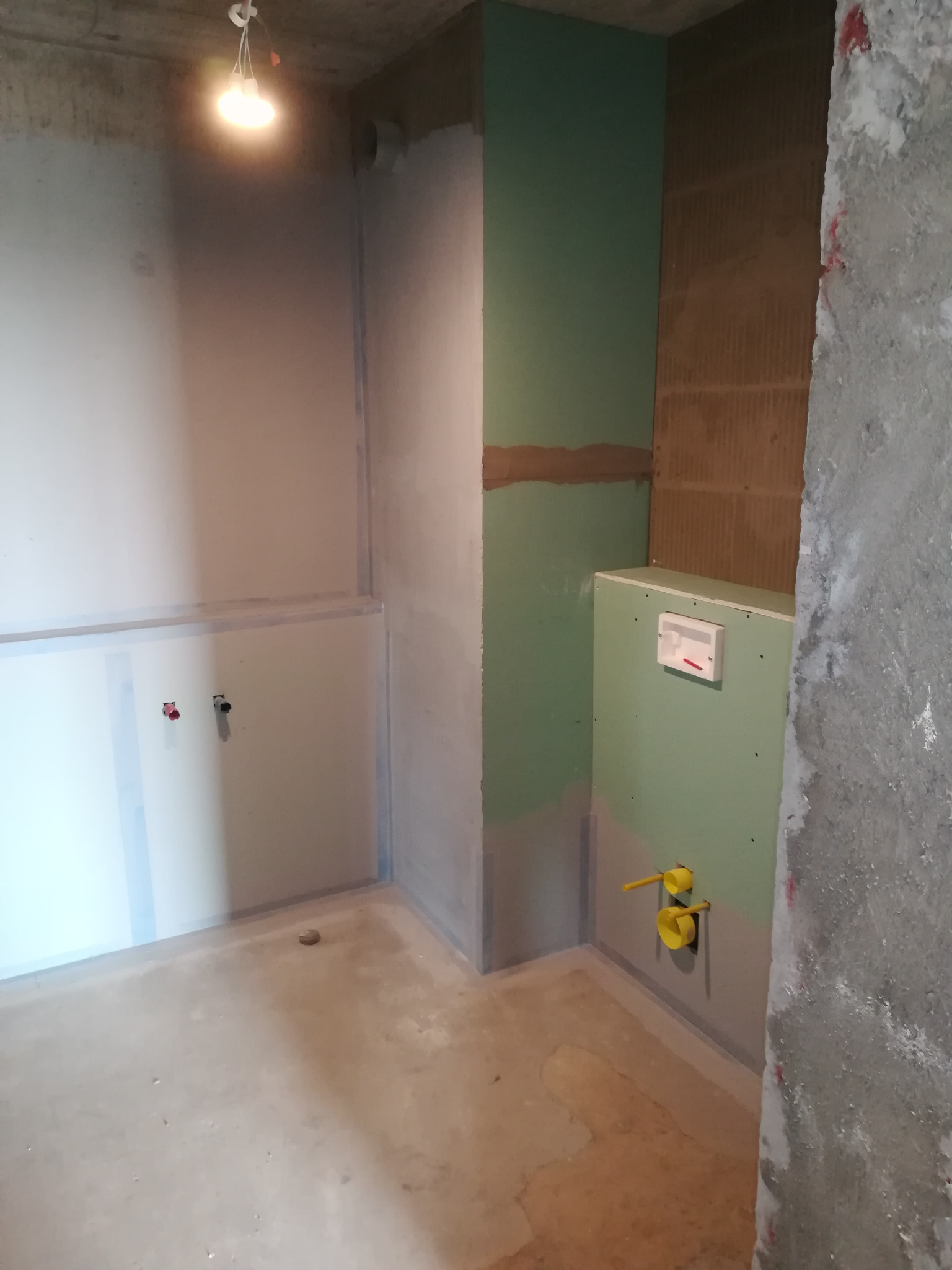 Wnętrze łazienki w trakcie prac w Wielkich Drogach. Widoczne płyty karton-gips, instalacja wodna i fragment surowej ściany. Etap przygotowania do dalszych prac wykończeniowych.