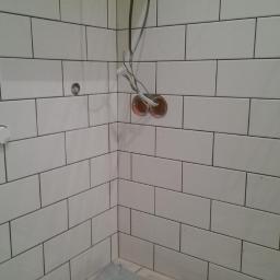 Professional Job Usługi Remontowe-Budowlane - Wykończona ściana w łazience z białymi, podłużnymi płytkami. Widoczne wystające kable i puszki elektryczne przed montażem osprzętu. Minimalistyczny styl.