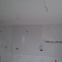 Professional Job Usługi Remontowe-Budowlane - Wnętrze w trakcie wykańczania: białe, heksagonalne płytki częściowo ułożone na ścianie, widoczne instalacje elektryczne, surowy stan wykończenia.