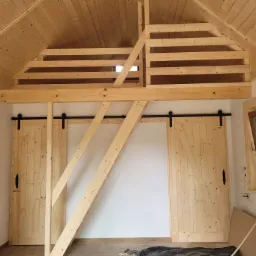 Wnętrze z drewnianą antresolą w trakcie budowy w Juszczynie, widoczne przesuwne drzwi stodołowe i drewniane wykończenie poddasza.