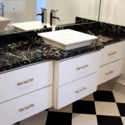 Łazienka z czarnym blatem z białymi żyłkami, białą umywalką nablatową, białymi szafkami z ozdobnymi uchwytami i podłogą w czarno-białą szachownicę.