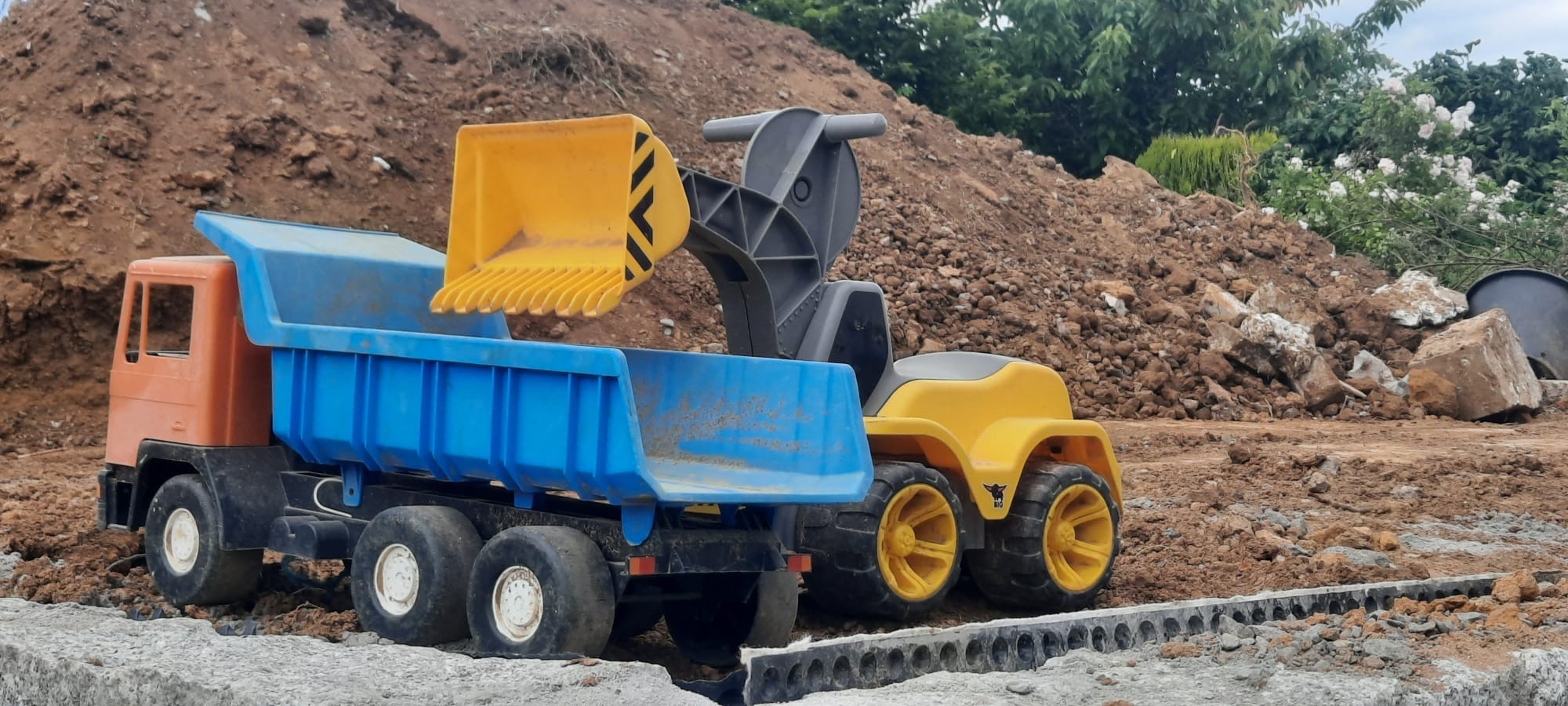 Zabawkowy samochód ciężarowy z koparką na tle ziemi i kostki w Wólce Pełkińskiej. Model budowlany dla dzieci, imitujący prace ziemne i transport materiałów.