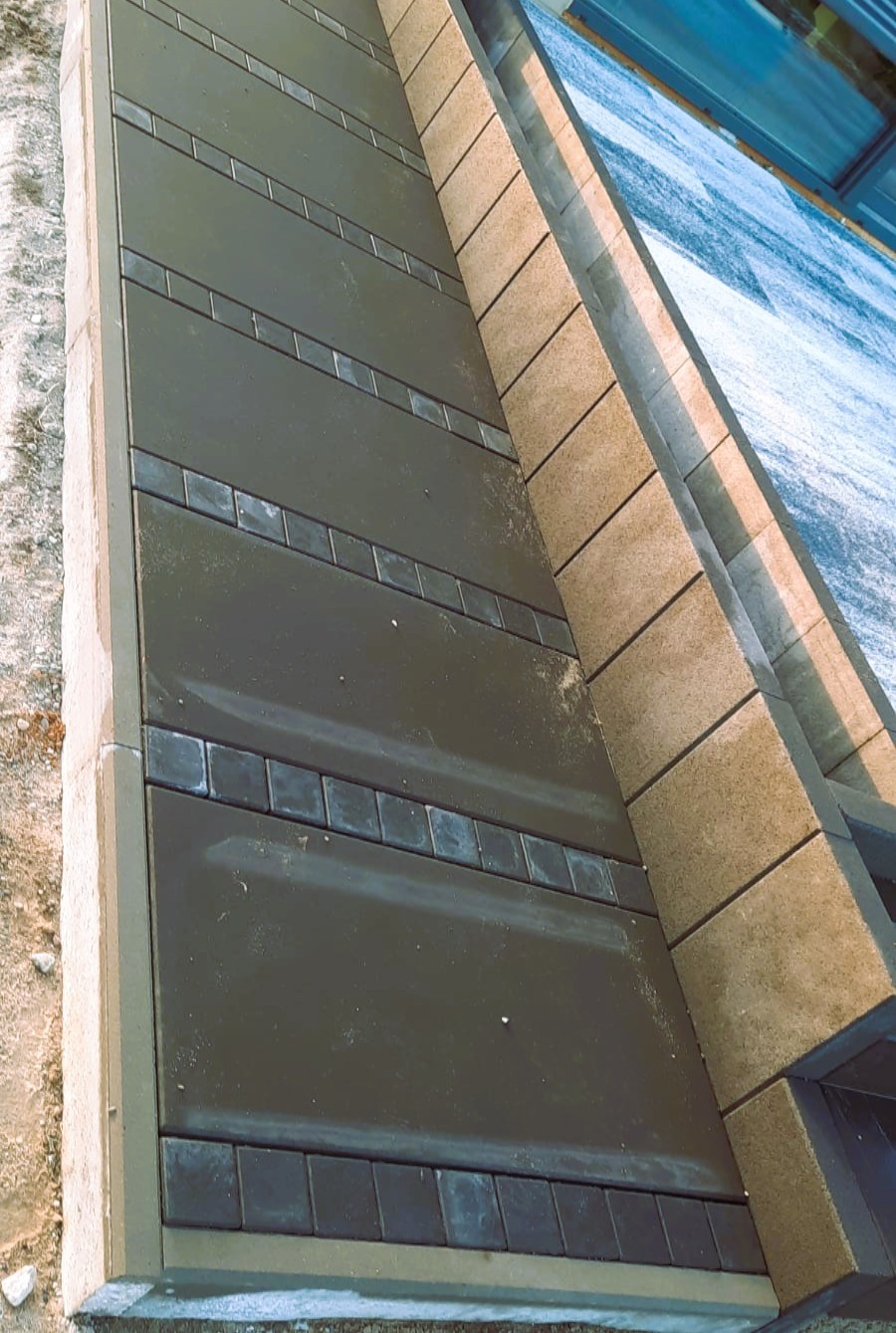 Ukończona nawierzchnia z ciemnej kostki z dekoracyjnymi wstawkami, obrzeża z jasnej kostki. Widok z góry, ukośne ujęcie.