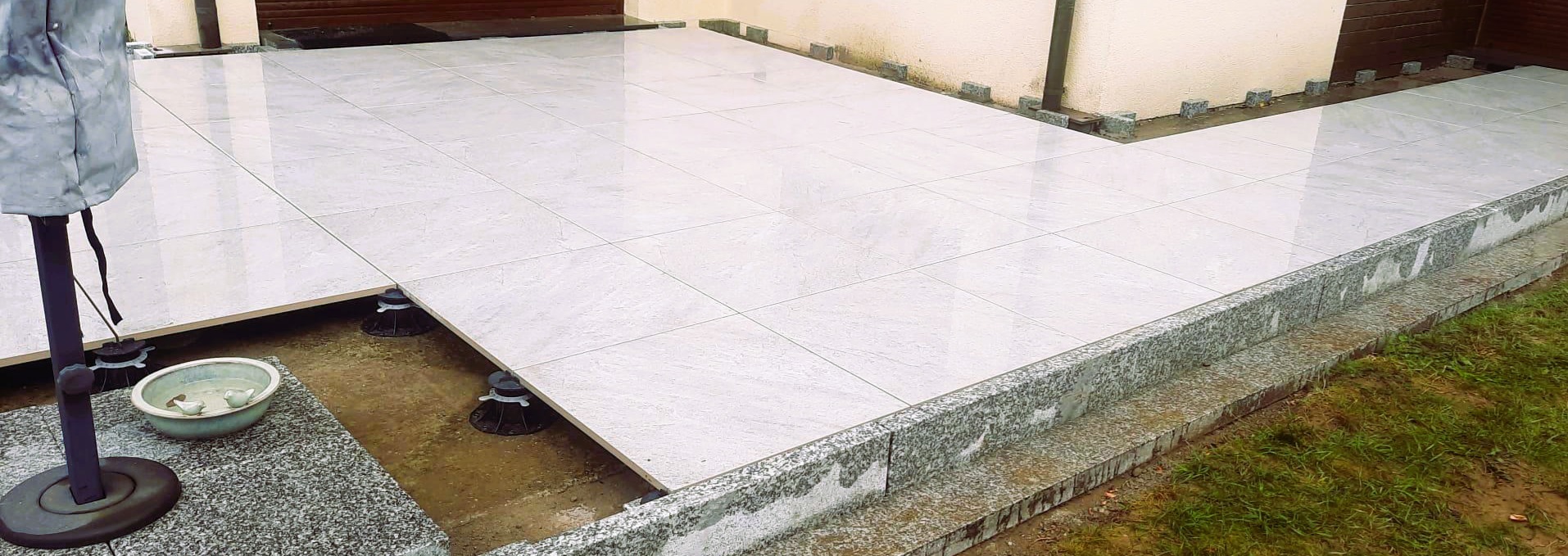 Jasnoszary taras z płytek na regulowanych wspornikach, obrzeża z granitu. Widoczne elementy konstrukcyjne tarasu.