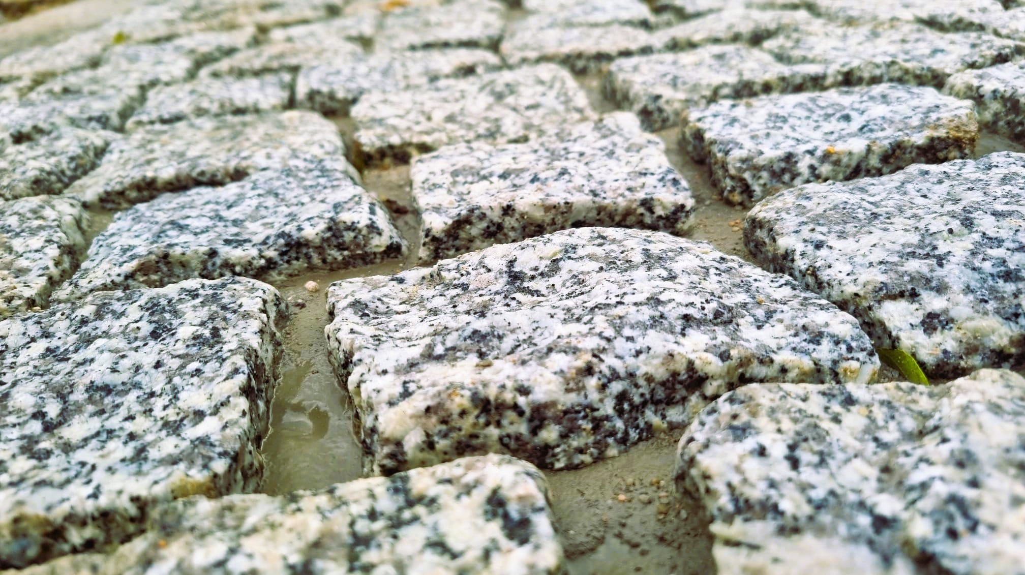 Ułożona, szara kostka granitowa z bliska, z widocznymi fugami, Wólka Pełkińska. Kamień o nieregularnej fakturze, tworzący trwałą nawierzchnię.