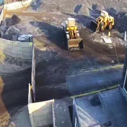 Plac składowy z dwoma żółtymi ładowarkami kołowymi pracującymi przy hałdach materiału, widok z góry.