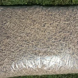 Worek przezroczystej folii wypełniony pelletem drzewnym, leżący na zielonej trawie.