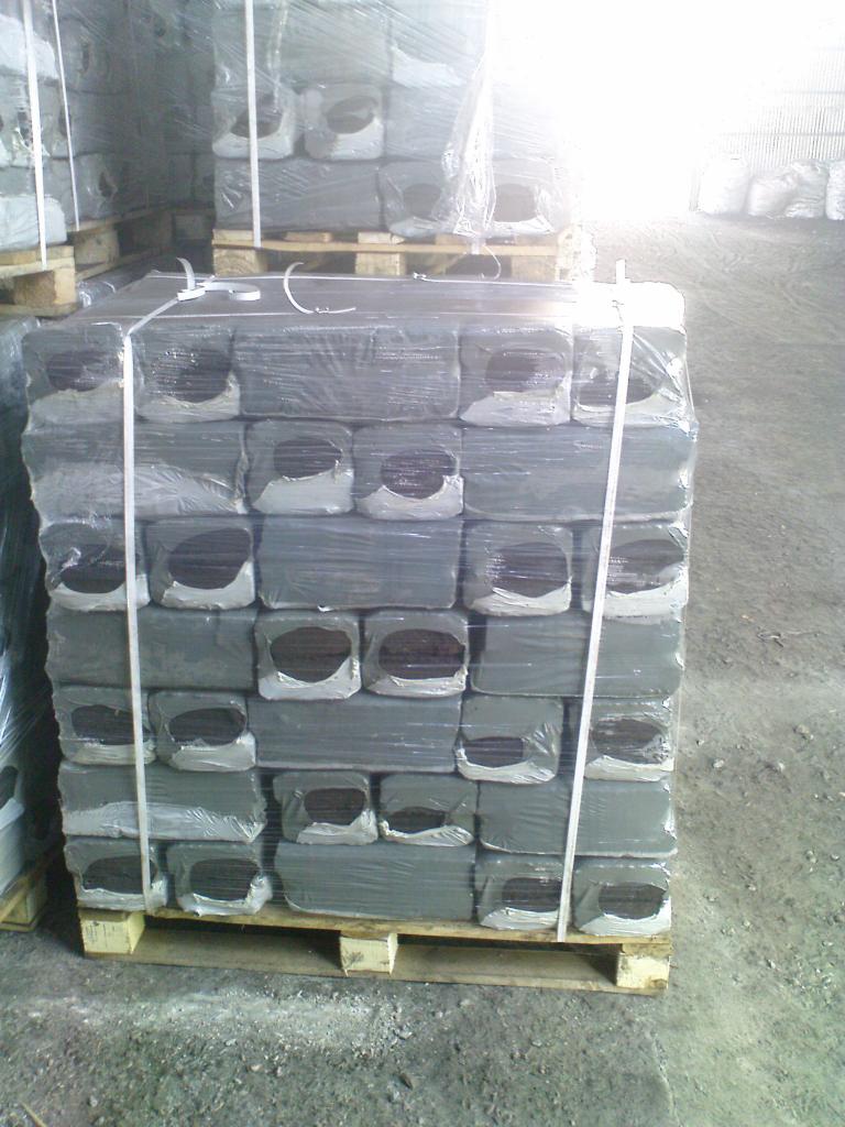 Paleta brykietu torfowego, owinięta folią, z widocznymi otworami w każdym bloku, składowana w magazynie.