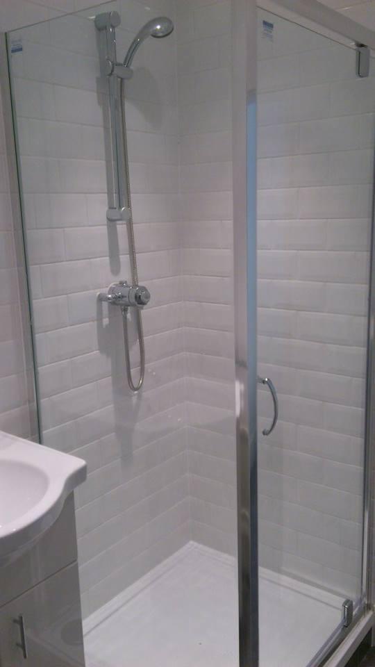 Kabina prysznicowa z chromowaną armaturą i białymi, prostokątnymi płytkami ułożonymi poziomo, widok z boku umywalki.