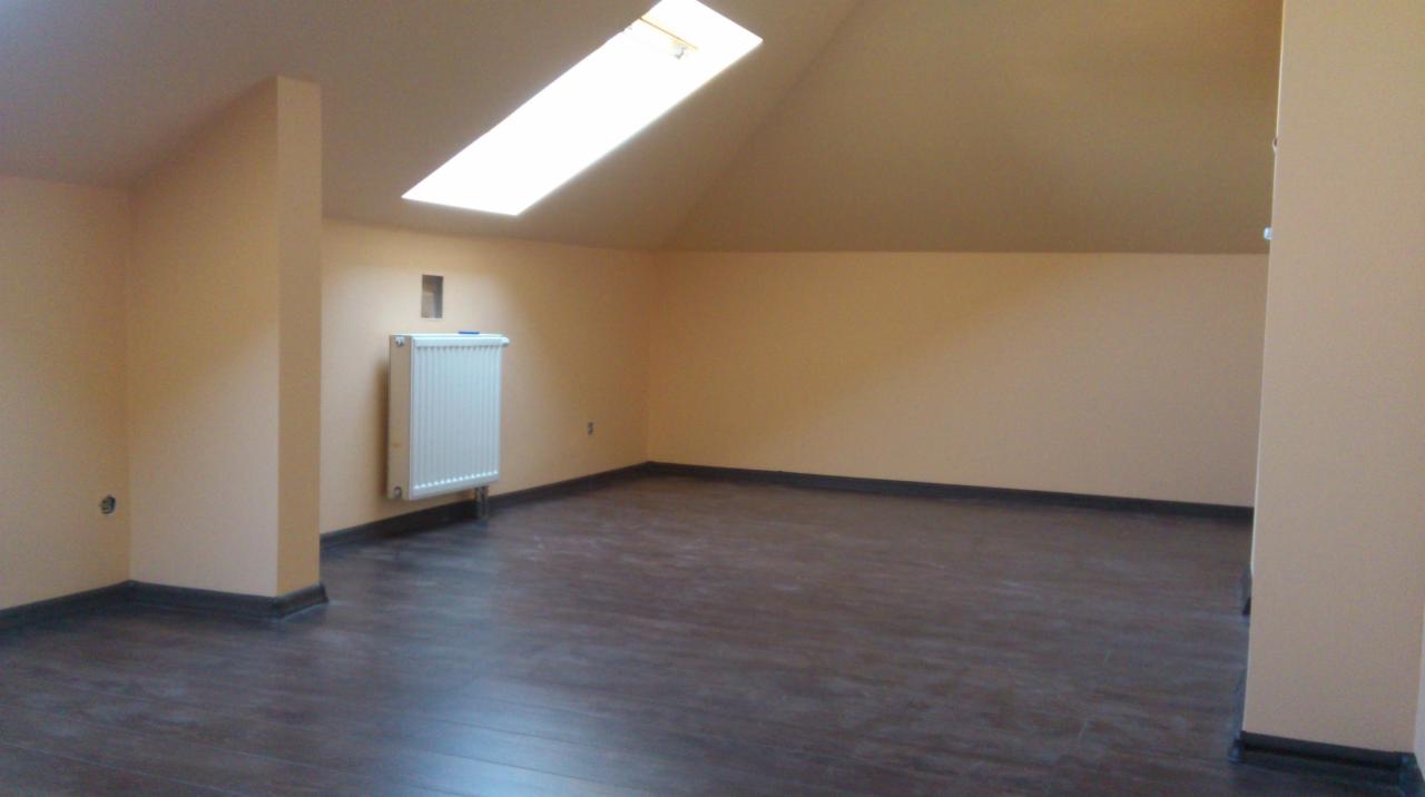 Poddasze po remoncie z drewnopodobną podłogą, beżowymi ścianami, białym grzejnikiem i oknem dachowym.