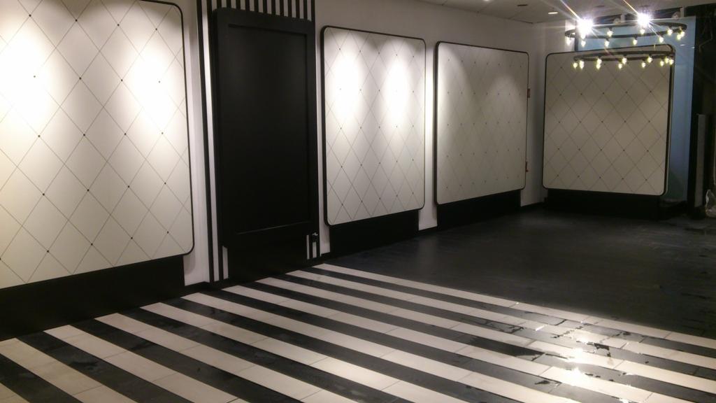 Wnętrze z panelami ściennymi w romby i czarno-białą podłogą w pasy, oświetlone punktowo