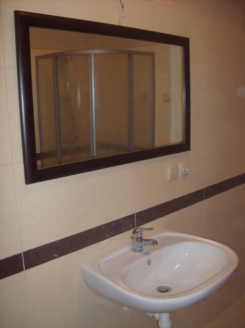 Łazienka z umywalką, lustrem z brązową ramą, w którym odbija się kabina prysznicowa; beżowe płytki z brązowym paskiem dekoracyjnym.