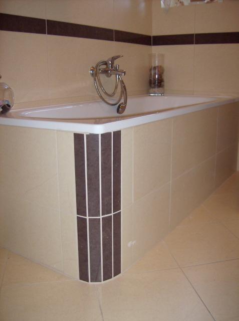 Wykończona łazienka z obudowaną wanną w beżowych płytkach z brązowymi akcentami, widoczna bateria wannowa i dekoracyjny wazon.