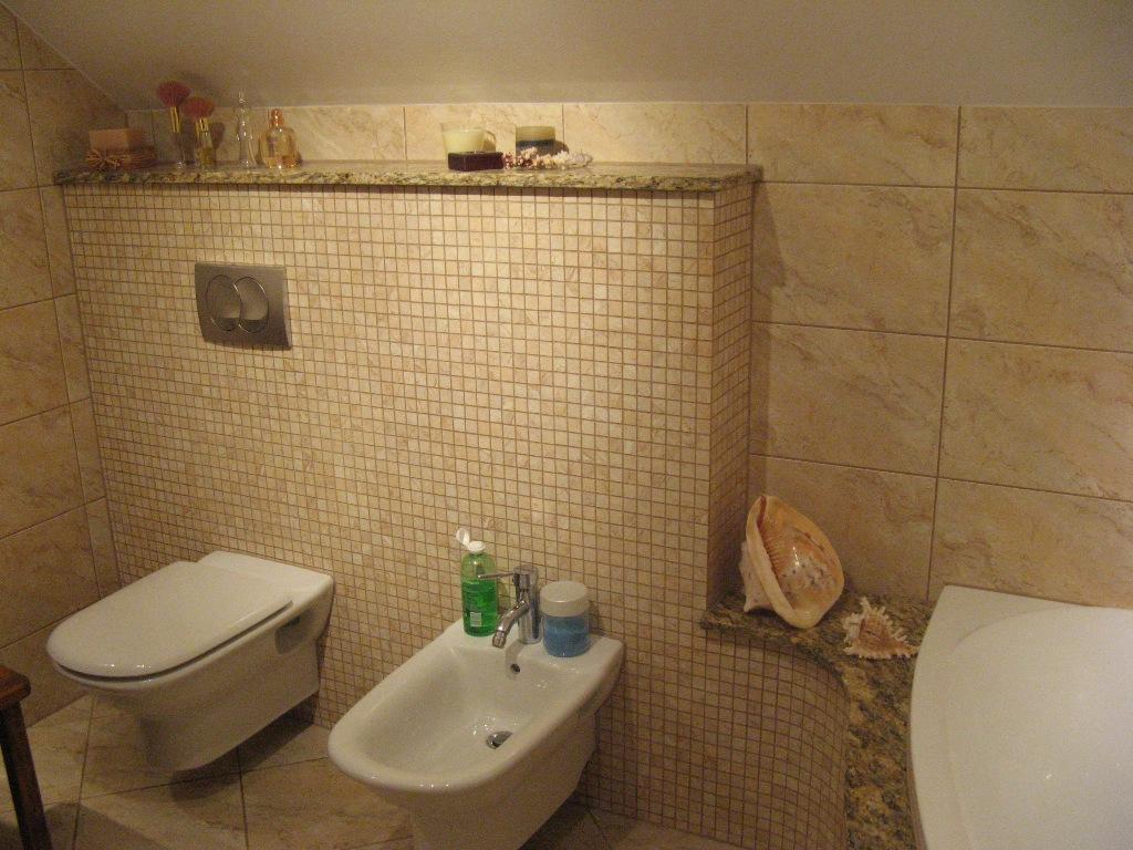 Łazienka wykończona beżowymi mozaikowymi płytkami, z wiszącą toaletą, bidetem, wanną i dekoracjami z muszli na półce.