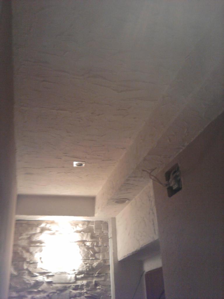 Wykończone wnętrze z dekoracyjnym tynkiem na suficie i ścianie, oświetleniem punktowym i fragmentem ściany z imitacją kamienia, widok z dołu.