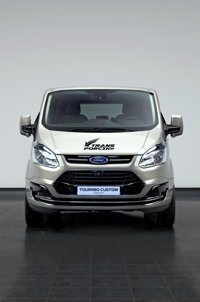 Przód srebrnego Forda Tourneo Custom z naklejką 'TRANS PORCIKO' na masce, zaparkowanego na ciemnej posadzce przed szarym tłem.