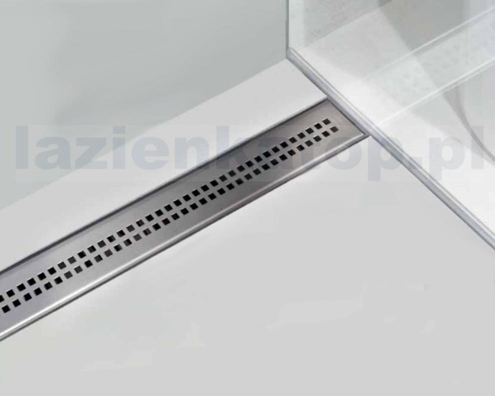 Szczegółowe ujęcie liniowego odpływu podłogowego Alcaplast w kabinie prysznicowej z białym brodzikiem i szklaną ścianką.
